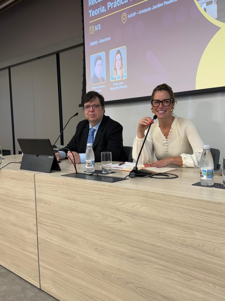 Foto com a presidente Paula Lima Hyppolito Oliveira e o Coordenador do Curso Gilberto Gomes Bruschi na Unidade Jardim Paulista, sentados na mesa. E Paula está falando ao microfone